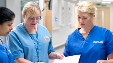 Three women in blue scrubs discussing a file