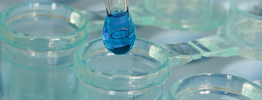 A dropper of blue liquid being emptied into a glass jar.