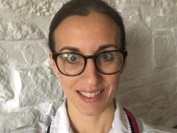 A woman wearing a white hospital uniform, stethoscope and glasses
