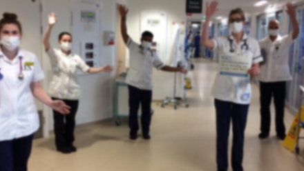A group of physiotherapists in a hospital corridor holding their hands up