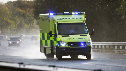 An ambulance with blue lights lit driving on a rainy motorway