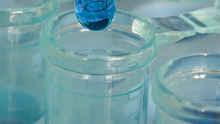 A dropper of blue liquid being emptied into a glass jar.