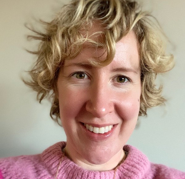 A woman with curly blonde hair wearing a pink jumper