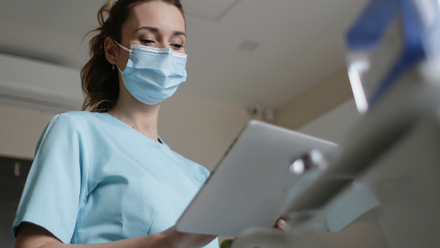 A woman wearing a mask looking at a laptop
