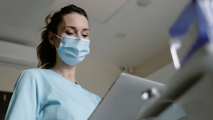 A woman wearing a mask looking at a laptop