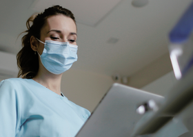 A woman wearing a mask looking at a laptop
