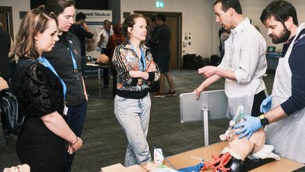 Five people stand together discussing the model on the table in front of them.