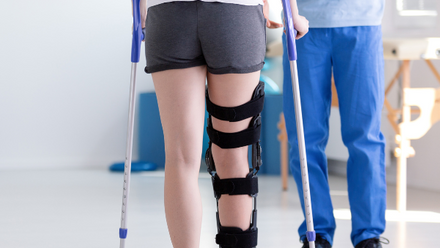 A person walks using crutches and knee brace