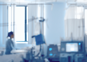 A person sits on a hospital bed in an empty room looking out the window