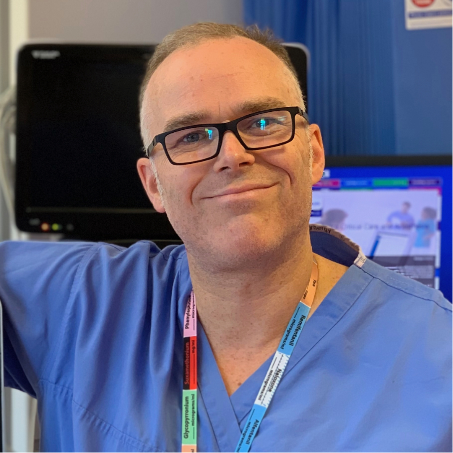 Photo of a man smiling wearing glasses and in hospital scrubs