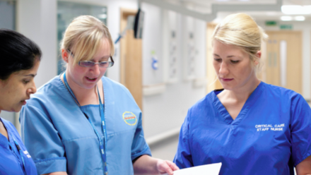 Three women in blue scrubs discussing a file